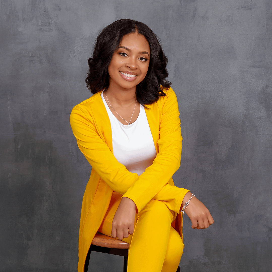 Woman in a yellow suit posing for business headshots pictures on a charcoal background.