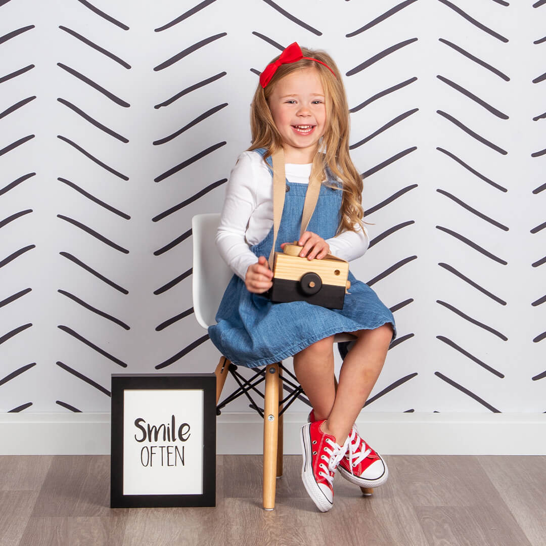 Girl smiling for professional children photos on a Herringbone background at JCPenney Portraits.