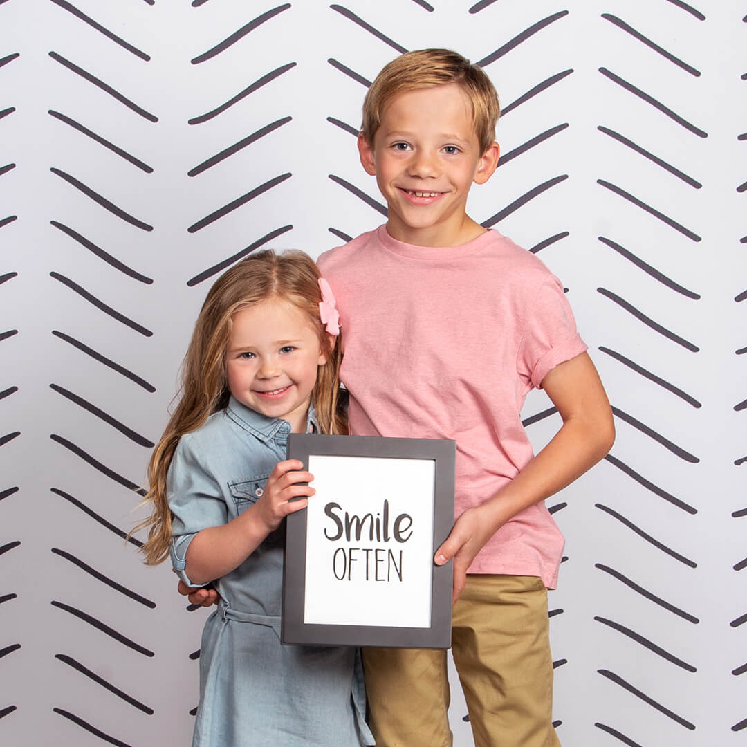 Siblings smiling for professional children photos on a Herringbone background at JCPenney Portraits.