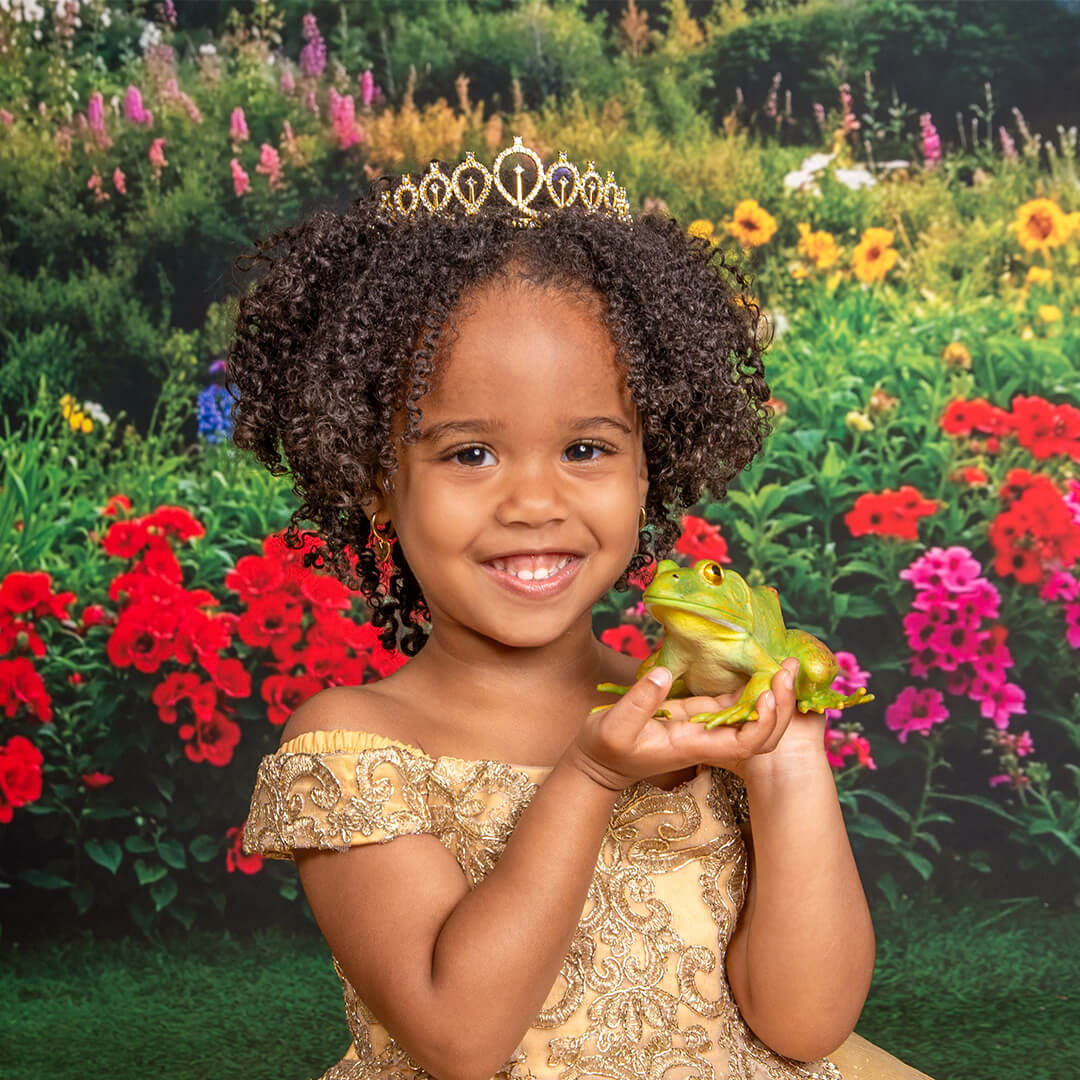 Girl in a tiara and gold princess gown holding a frog prop.