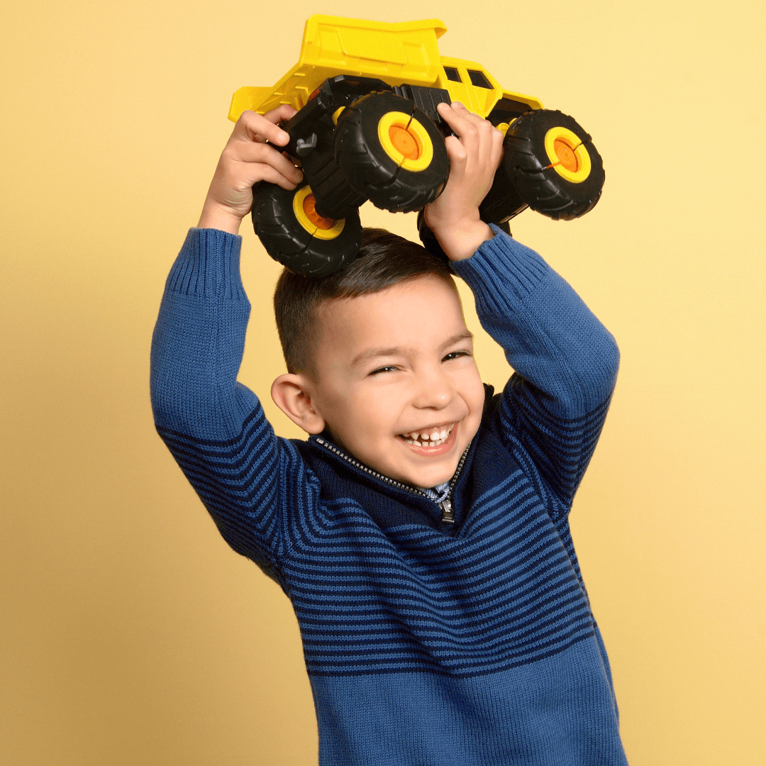 Boy holding a yellow toy truck posing for pictures on a yellow background.