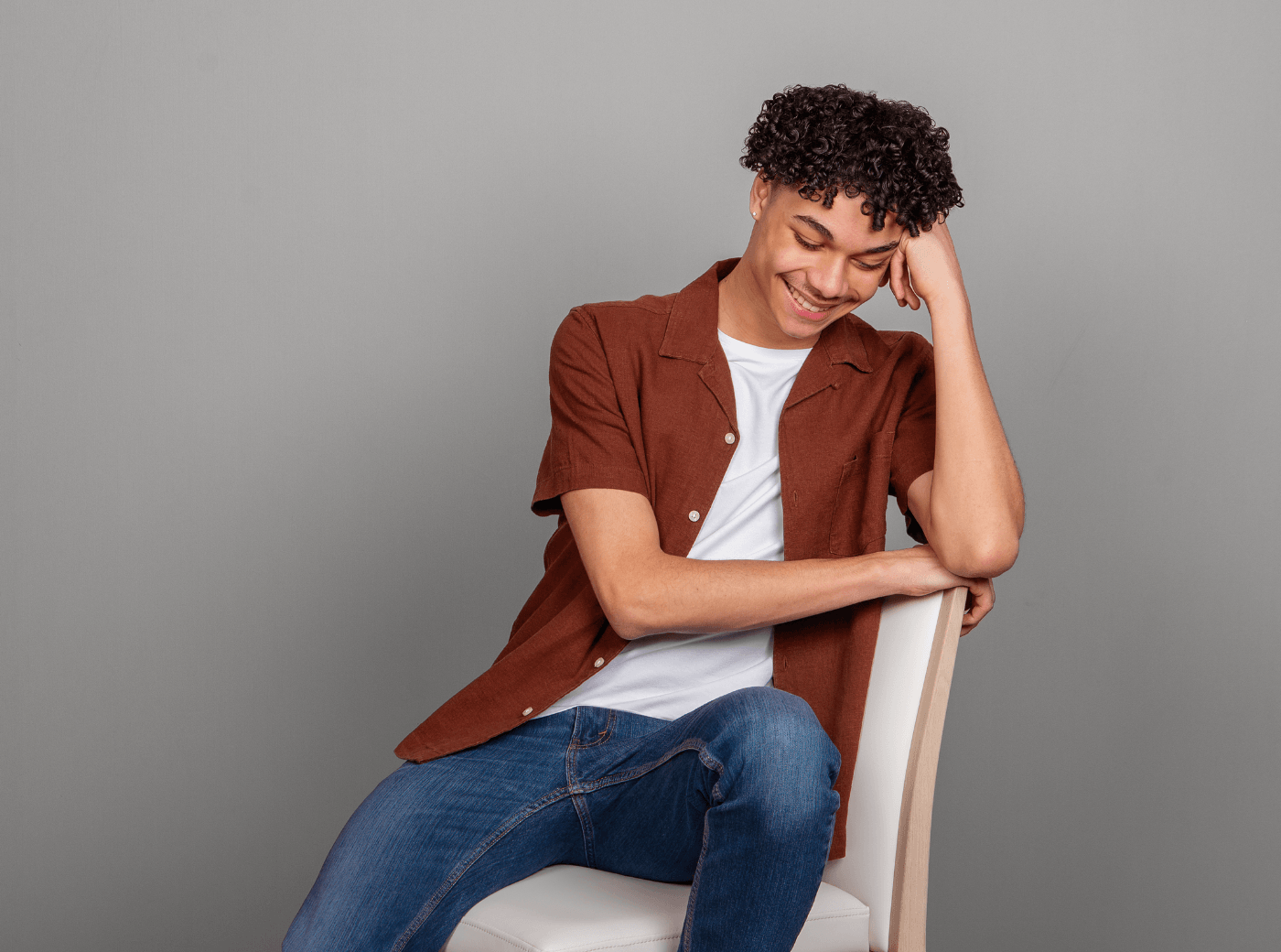 Senior male in a maroon button down and jeans posing on a chair for senior pictures.