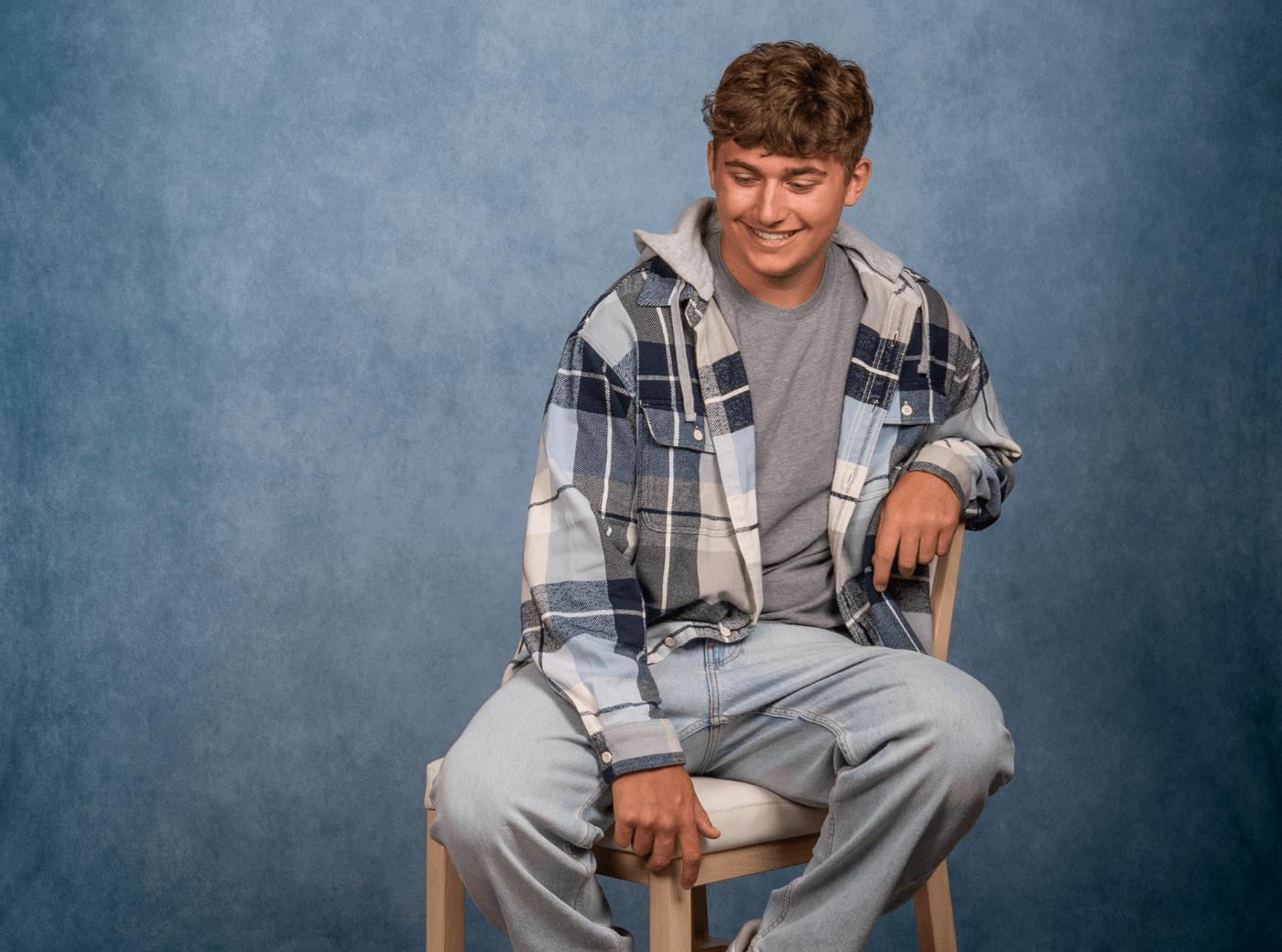 Senior male in a plaid jacket posing on a stool for professional senior pictures.