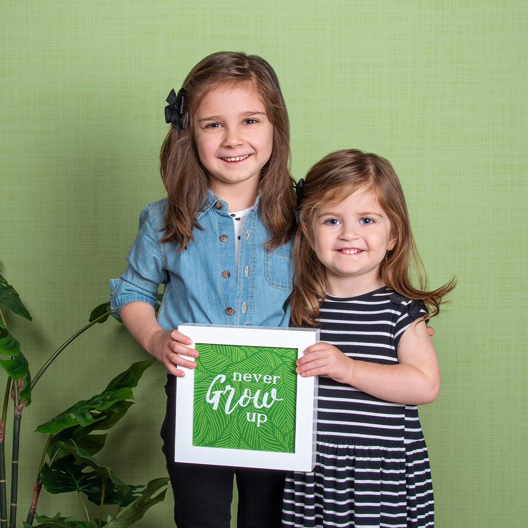Sisters smiling for professional children pictures on Willow background at JCPenney Portraits.