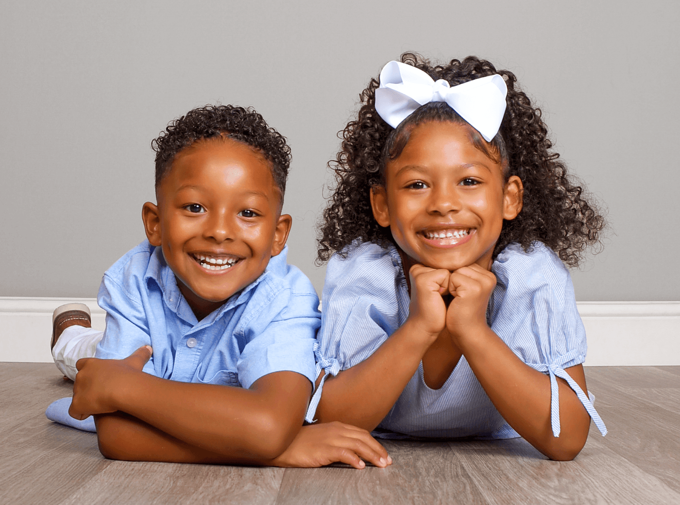 Siblings in blue outfits smiling for professional children photos at JCPenney Portraits.