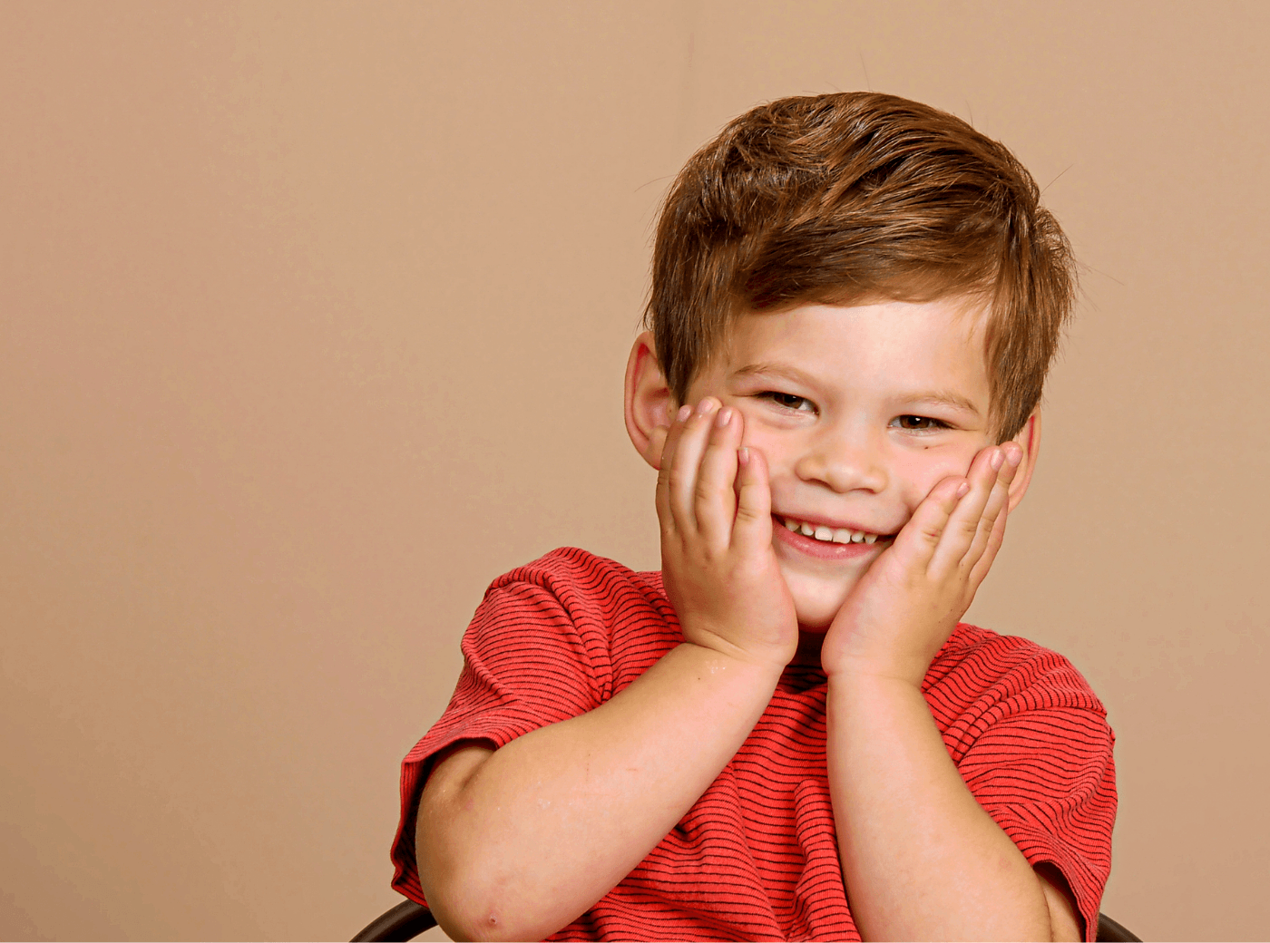 Boy in a red t-shirt with his hands on his face for professional child photography.