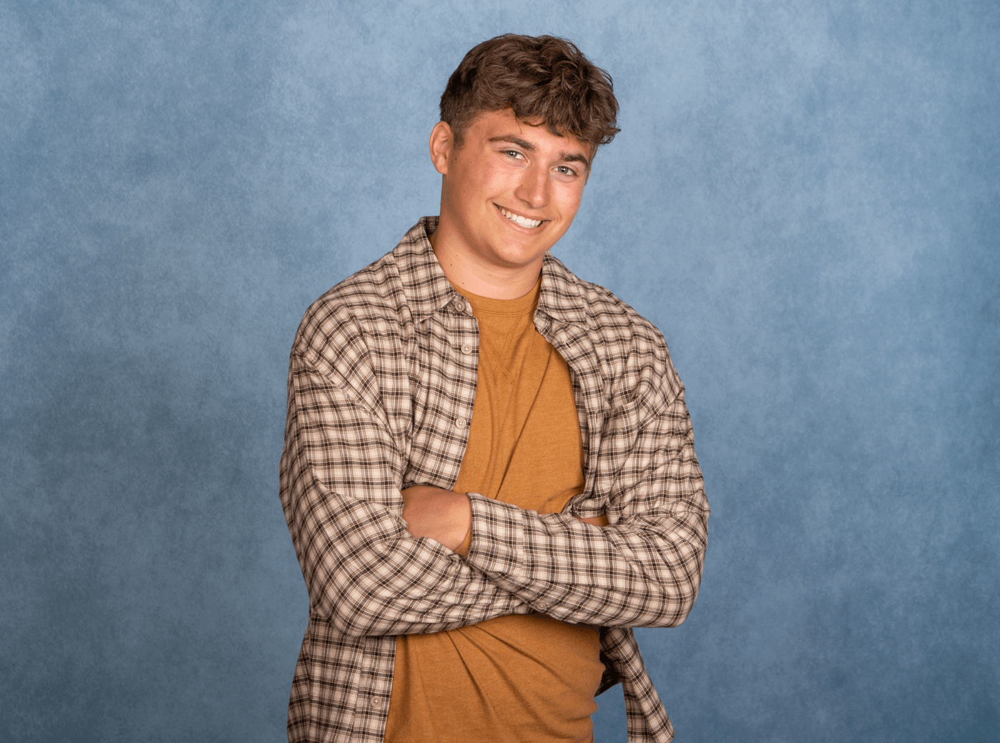 Senior male in a plaid button down on a blue background for professional senior pictures.