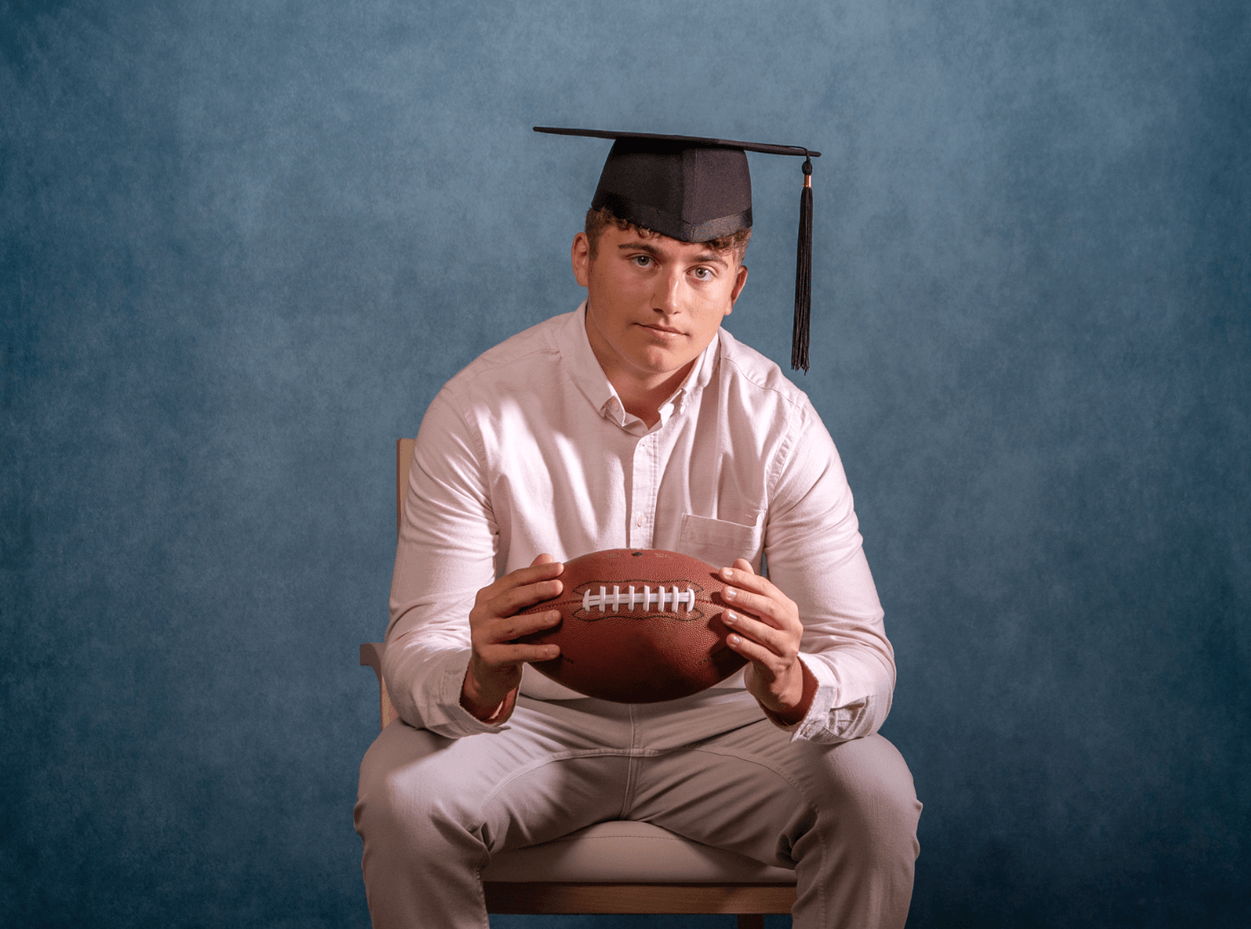 Graduating senior holding a football for professional graduation pictures at JCPenney Portraits.