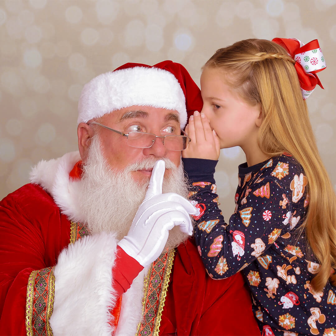 Girl whispering into Santa's ear for a Santa photography session at JCPenney Portraits.