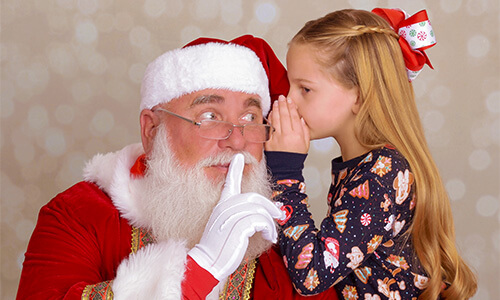 Girl whispering in Santa's ear for pictures with Santa at JCPenney Portraits.